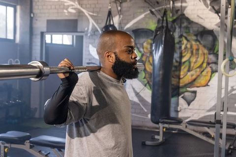 African american man lifting barbell across shoulders in urban gym with colorful mural