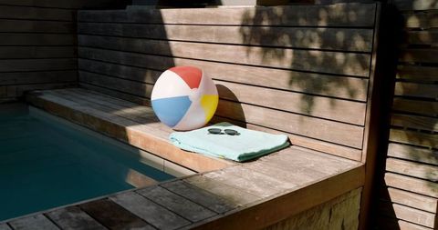 Colorful beach ball and sunglasses on poolside bench