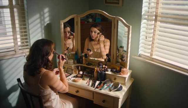 Woman applying makeup at vintage tri-fold vanity, sunlit morning beauty routine