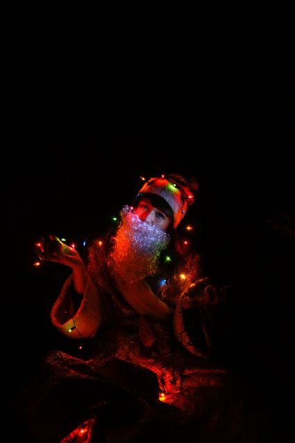 Santa Claus adorned with colorful Christmas lights in dark room, creating enchanting holiday atmosphere. Great for promoting Christmas events, advertising festivals, decorating catalogs, and holiday-themed marketing materials.
