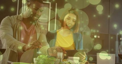 Couple cooking together sharing recipe on tablet while seasoning salad in modern kitchen