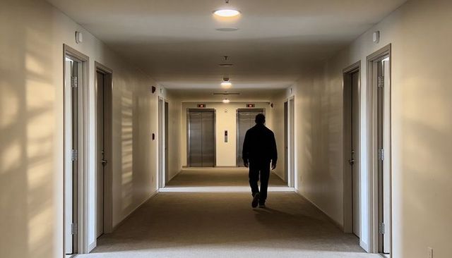 Walking silhouette in quiet hotel corridor toward elevators with strong shadow lines and symmetry