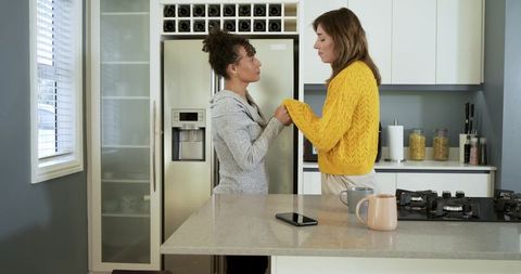 Two women holding hands in modern kitchen sharing tender conversation and quiet support