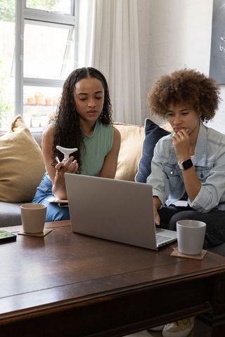 Two african american women collaborating on laptop at home, remote work and research planning