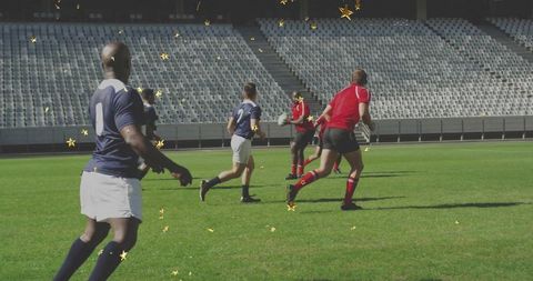 Sprinting red-shirted player carrying rugby ball toward navy defenders in empty stadium