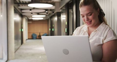 Professional Woman Typing on Laptop in Modern Office Corridor