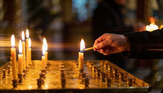 Hand lighting votive candle at church altar, warm golden glow on brass candle tray