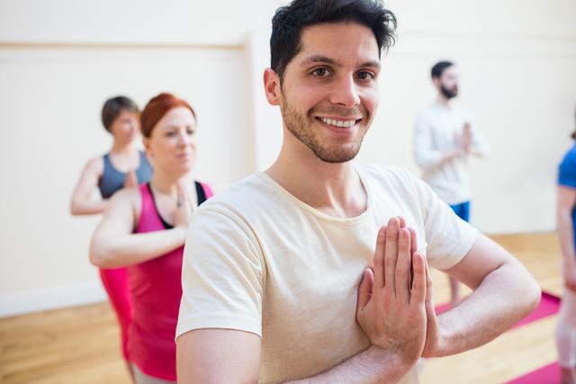 Group of people practicing tree pose in a yoga class. They are standing in a fitness studio with wooden floors, focusing on balance and mindfulness. This image is ideal for promoting yoga classes, wellness programs, fitness studios, and healthy lifestyle campaigns.