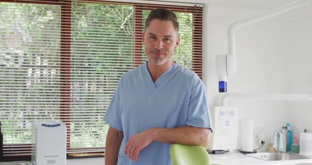 Male dentist in modern dental office smiling confidently. Ideal for use in healthcare articles, promotional material for dental clinics, illustrating a welcoming and professional atmosphere in medical settings.