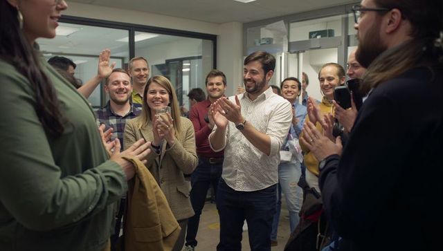 Startup team celebrating promotion in office corridor applauding coworker with smartphones