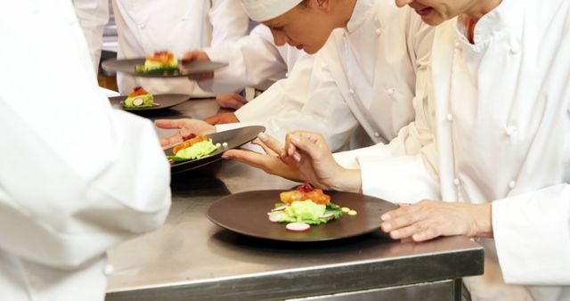 Chefs in white uniforms carefully decorating food plates with precision. Suitable for themes related to culinary arts, professional kitchens, teamwork in restaurants, gastronomy, and food presentation techniques.