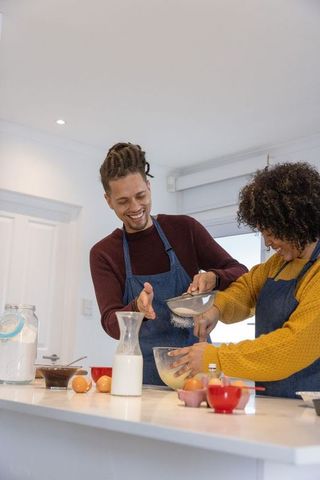 African american couple baking together in modern kitchen sifting flour and laughing