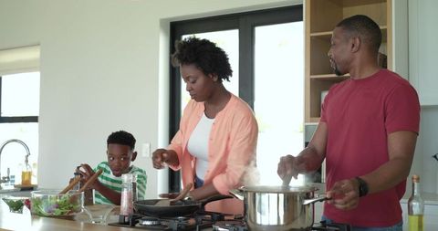 African American family cooking together at kitchen island preparing meal tossing salad