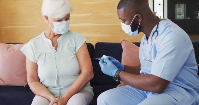 Image of african american male doctor in face mask vaccinating caucasian senior woman. seniors health and nursing home lifestyle concept.