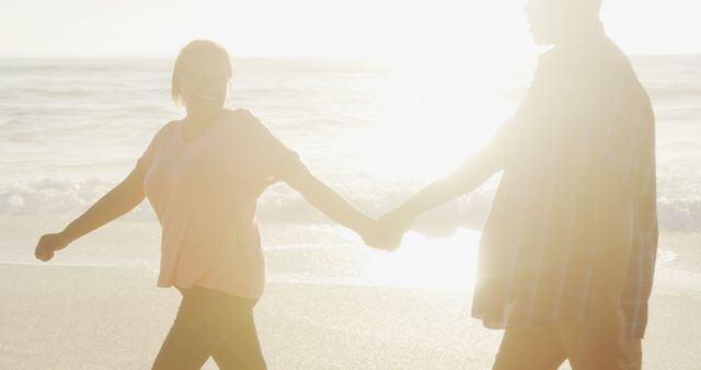 Smiling senior african american couple holding hands and walking on sunny beach - Download Free Stock Photos Pikwizard.com