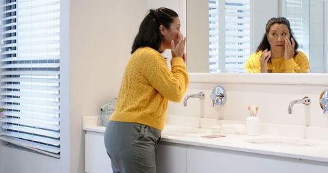 Woman applying face cream in modern bathroom