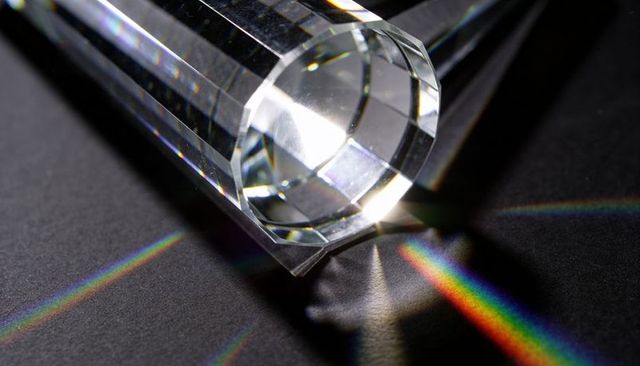 Faceted crystal prism dispersing bright white beam into vibrant rainbow spectra
