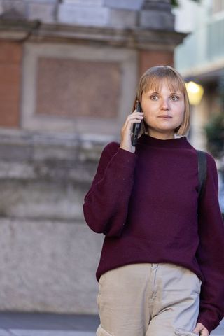 Woman walking and talking on phone near urban monument with maroon sweater and backpack