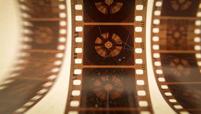 Vintage 35mm film strip macro backlit showing sprocket holes, dusty celluloid texture