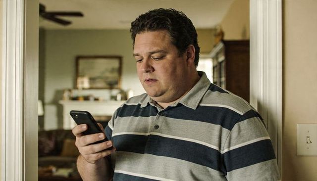 Man checking smartphone in doorway at home wearing striped polo, thoughtful domestic moment