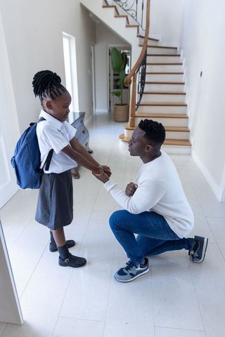 African american father kneeling and encouraging daughter before school with backpack