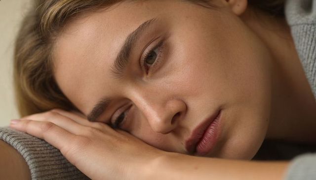 Contemplating young woman resting cheek on forearm in soft warm natural light