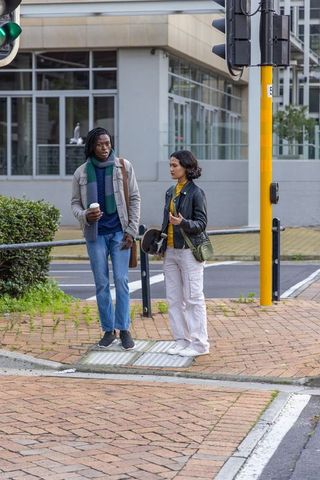Diverse couple chatting at urban crosswalk holding coffee cup and skateboard