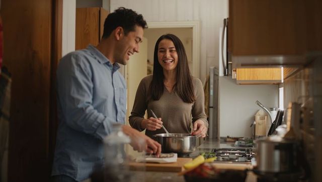 Couple cooking together at kitchen island chopping vegetables and stirring saucepan