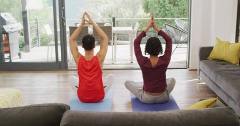 Couple practicing yoga and stretching on mats in bright living room with patio view