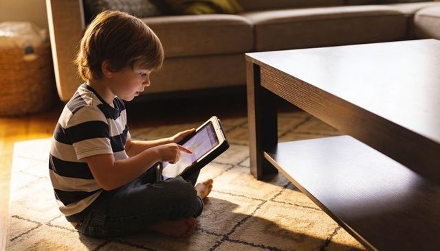 Sunlit living room child using tablet on patterned rug, striped tee, cozy tech play