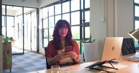 African american woman smiling and using smartphone at modern open-plan office desk