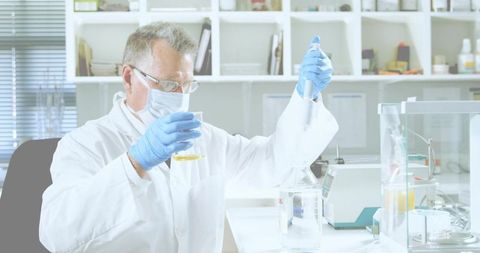 Senior researcher pipetting yellow solution at sunlit lab bench wearing ppe, gloves, goggles