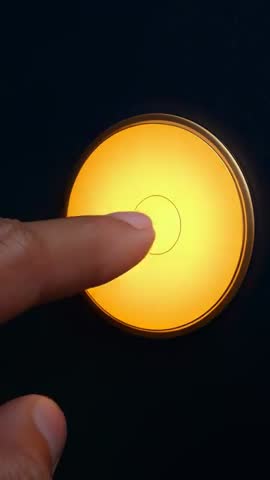 Finger Pressing Amber Touch Button on Dark Panel Vertical Video Close-Up