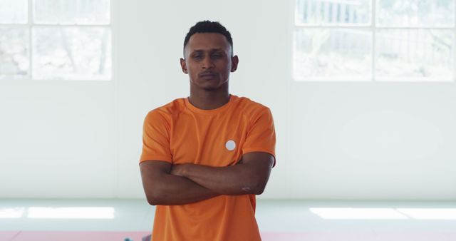 Confident Man in Orange Shirt Standing with Arms Crossed Indoors - Download Free Stock Images Pikwizard.com