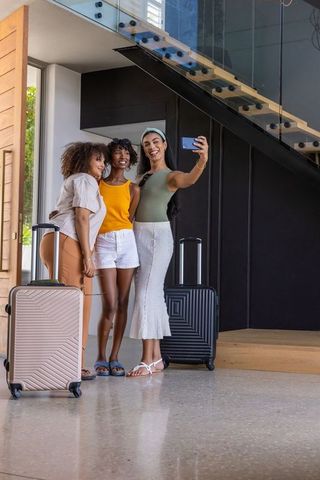 Multicultural friends taking selfie in modern hotel lobby with suitcases
