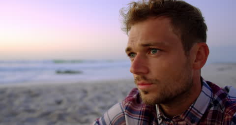 Pensive Man on Beach During Sunset with Vibrant Sky