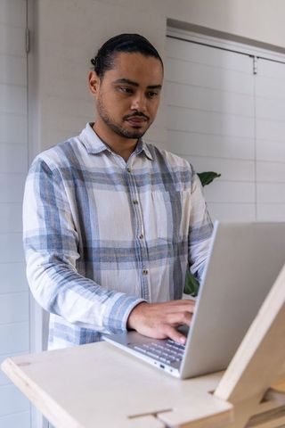 Asian man working at standing adjustable workstation typing on laptop in minimalist office