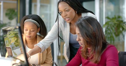 Diverse female team collaborating at desktop computer in modern glass office workspace