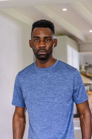 African american man standing in minimalist kitchen in blue t-shirt, serious