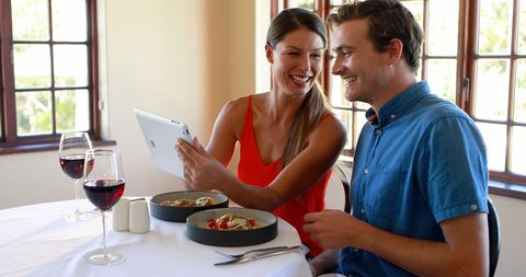 Joyful Couple Dining and Using Tablet in Sunlit Restaurant