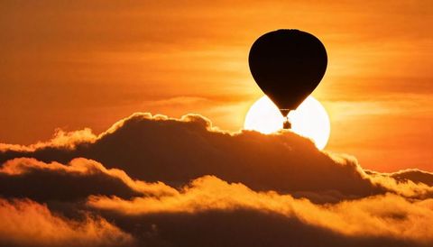 Hot air balloon drifting above golden cloud bank at sunrise dramatic silhouette