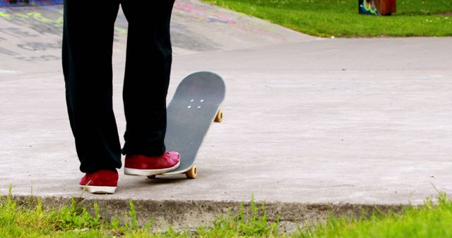 Image shows a person wearing red shoes standing in a skatepark, preparing to ride a skateboard. Ideal for use in content related to recreational sports, urban youth activities, skateboarding tutorials, or lifestyle blogs focusing on active hobbies.