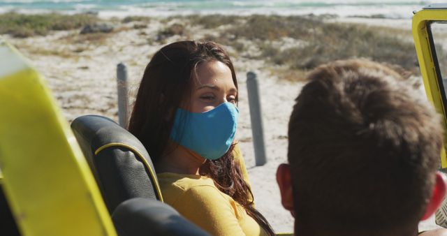 Young couple taking in beach scenery while wearing masks and traveling in convertible. Useful for promoting travel safety, COVID-19 precautions, and beach holidays. Captures essence of summer adventure during pandemic.