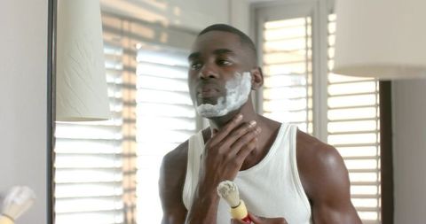 African American Man Applying Shaving Cream with Brush in Sunlit Bathroom Mirror