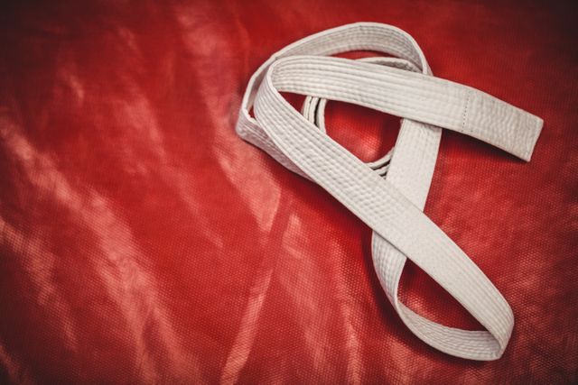 Close-up of a karate white belt placed on a red background. Ideal for use in articles or promotions related to martial arts training, beginner karate classes, sports equipment, fitness, and self-defense. The contrasting colors highlight the belt, symbolizing discipline and the start of a martial arts journey.