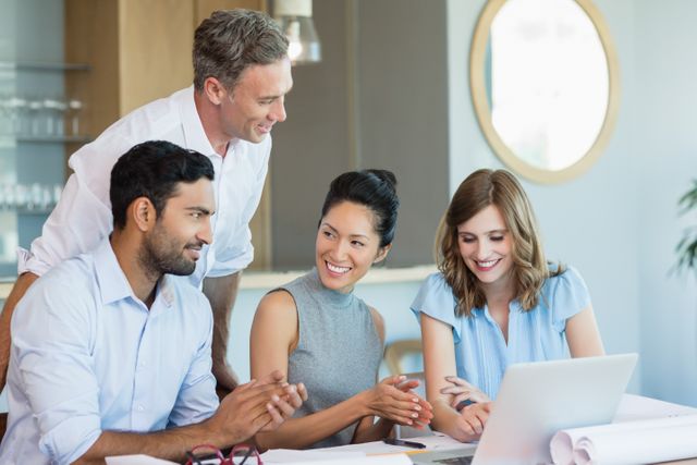Group of architects collaborating in a modern office environment. They are smiling and discussing ideas while looking at a laptop. This image can be used for promoting teamwork, professional collaboration, business meetings, and creative planning in a corporate setting.