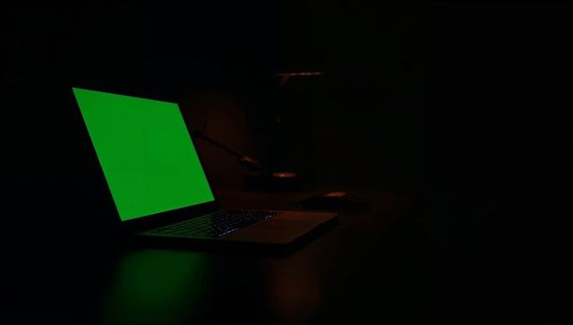 Laptop with green screen glow on backlit keyboard in low-light workspace for mockups