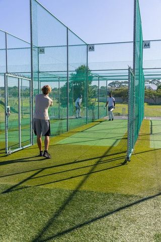 Cricket teammates practicing bowling and batting in outdoor net bays under bright sunlight