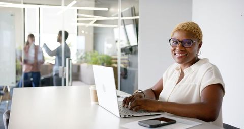 Confident Professional Woman Smiling While Working on Laptop in Modern Office