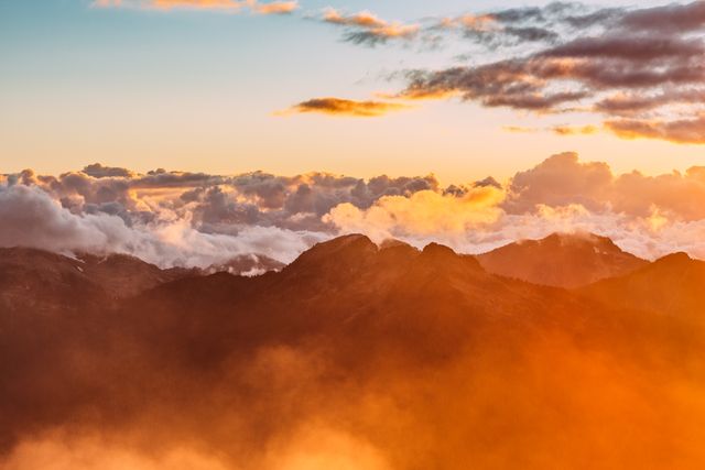 This depiction of a mountain range at sunrise features vibrant colors and hovering clouds, creating a stunning, picturesque landscape. Perfect for travel brochures, outdoor adventure promotions, nature websites, and inspirational posters to evoke feelings of awe and tranquility.
